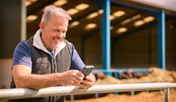 A man outside a farm building looking at a mobile phone.